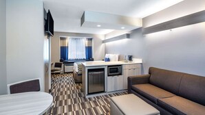 A compact hotel room with a kitchenette, a sofa, a dining table, and a TV mounted on the wall. - Microtel Inn & Suites by Wyndham Atlanta/Buckhead Area (Atlanta)