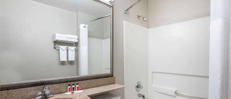 A bathroom with a granite countertop sink, a large mirror, a white toilet, and a bathtub.