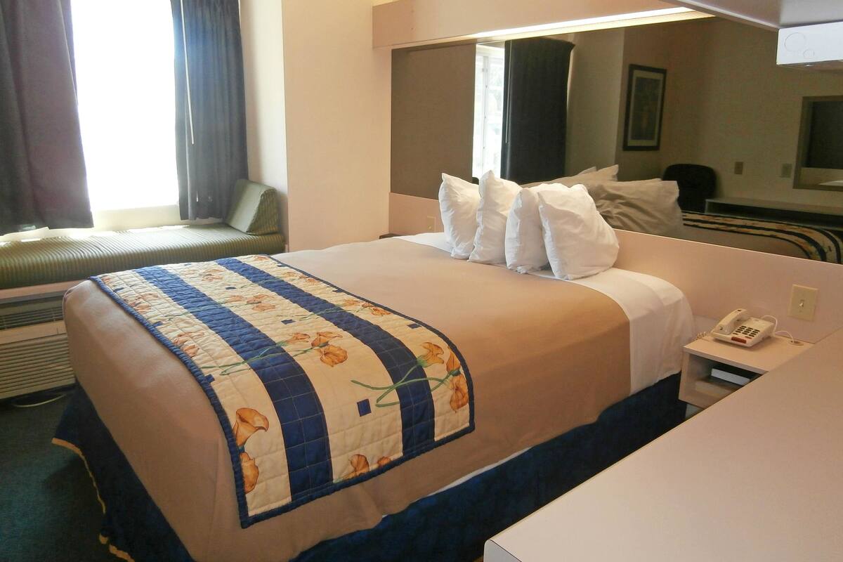 Ein Hotelzimmer mit einem Bett, einem Nachttisch mit Telefon, einem Fenster mit Vorhängen und einem Sessel am Fenster.