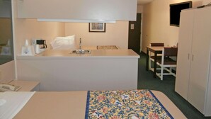 Una habitación de hotel compacta con cama, kitchenette pequeño, mesa de comedor y televisor.