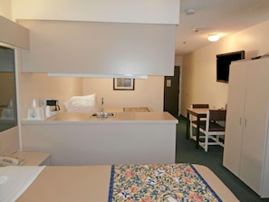 A compact hotel room with a bed, a small kitchenette, a dining table, and a TV. - Americas Best Value Inn And Suites Mcdonough (McDonough)