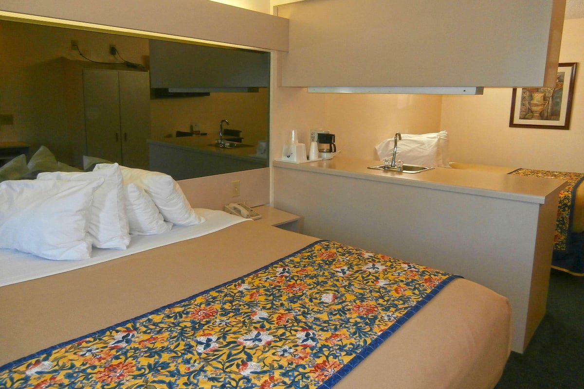 A hotel room with a bed, a small desk with a sink, and a mirror.