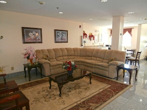 A living room with a sectional sofa, a coffee table, and a rug. There are framed pictures on the wall and a dining area in the background. - Americas Best Value Inn And Suites Mcdonough (McDonough)