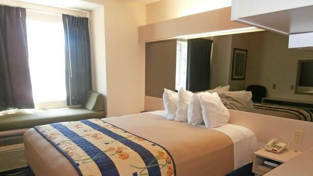Una habitación de hotel con una cama, una mesita de noche con teléfono y una ventana con cortinas.