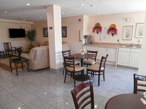 A dining area with a round table, chairs, a sofa, and a television mounted on the wall. - Americas Best Value Inn And Suites Mcdonough (McDonough)