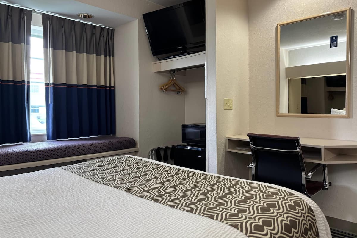 Una habitación de hotel con una cama, un escritorio con una silla, un televisor y un espejo.