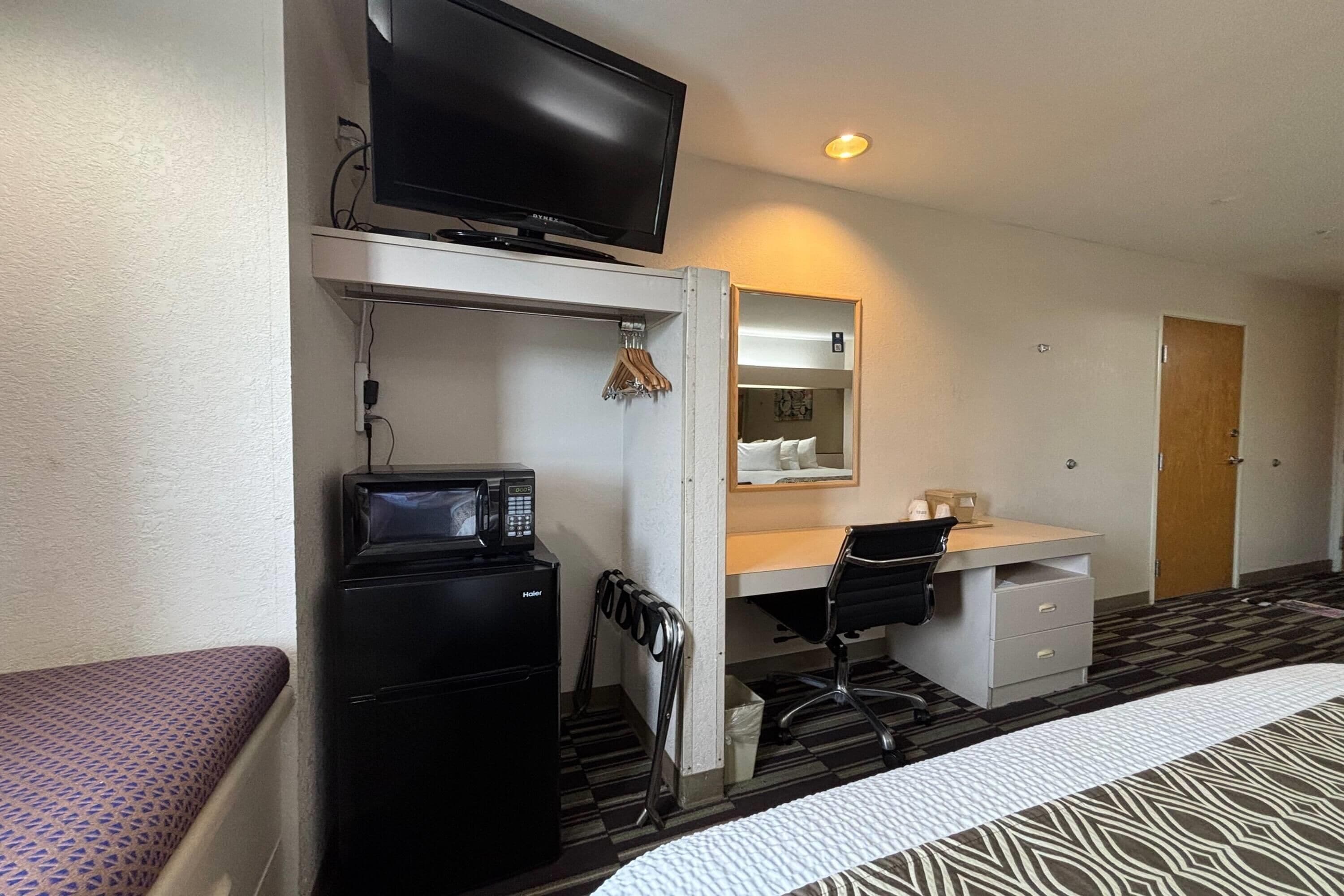 Habitación de hotel con cama, escritorio con computadora, microondas, televisión y armario.