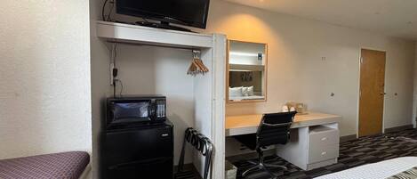 Habitación de hotel con cama, escritorio con computadora, microondas, televisión y armario.