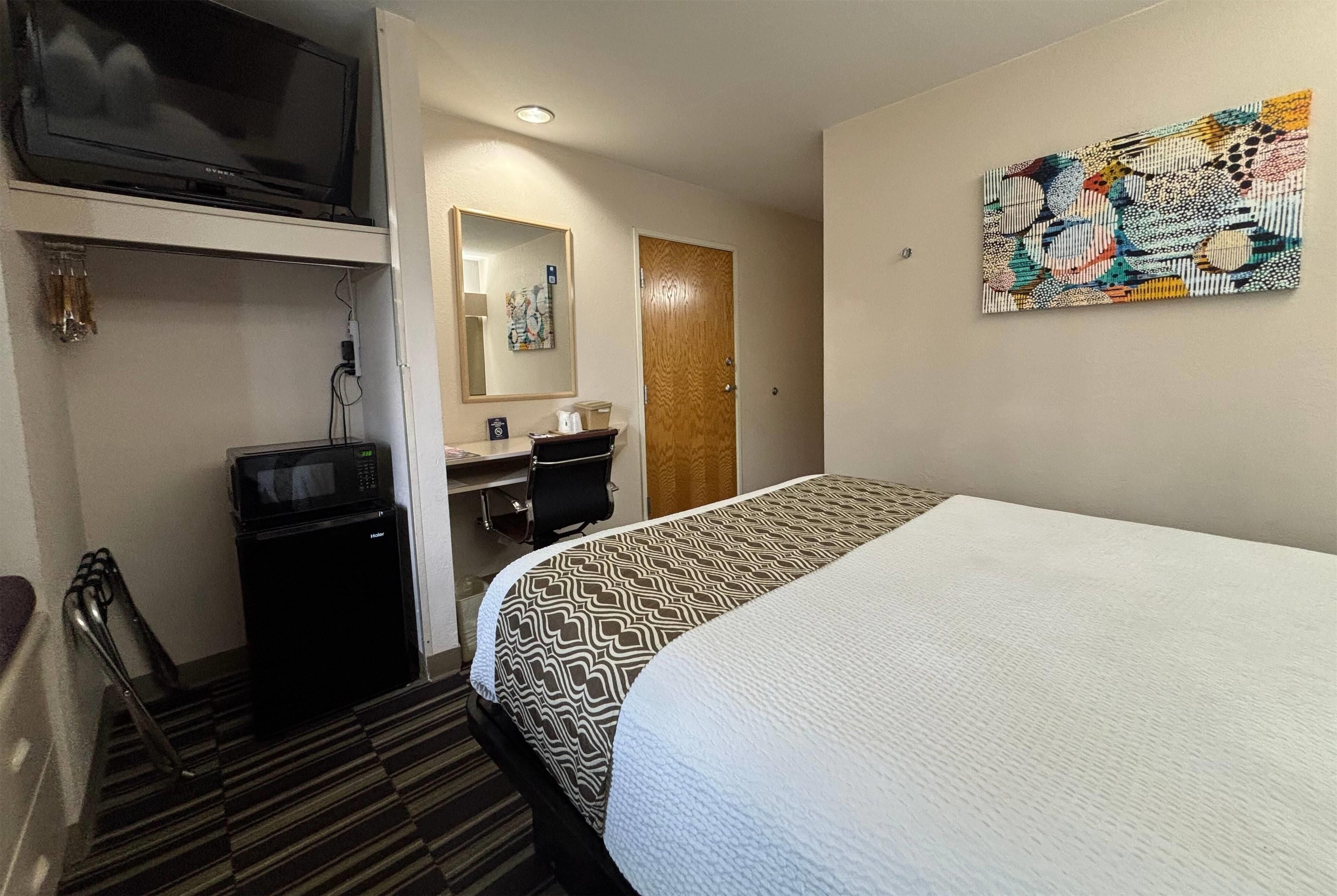 A hotel room with a bed, a TV, a desk with a chair, a microwave, and a door.