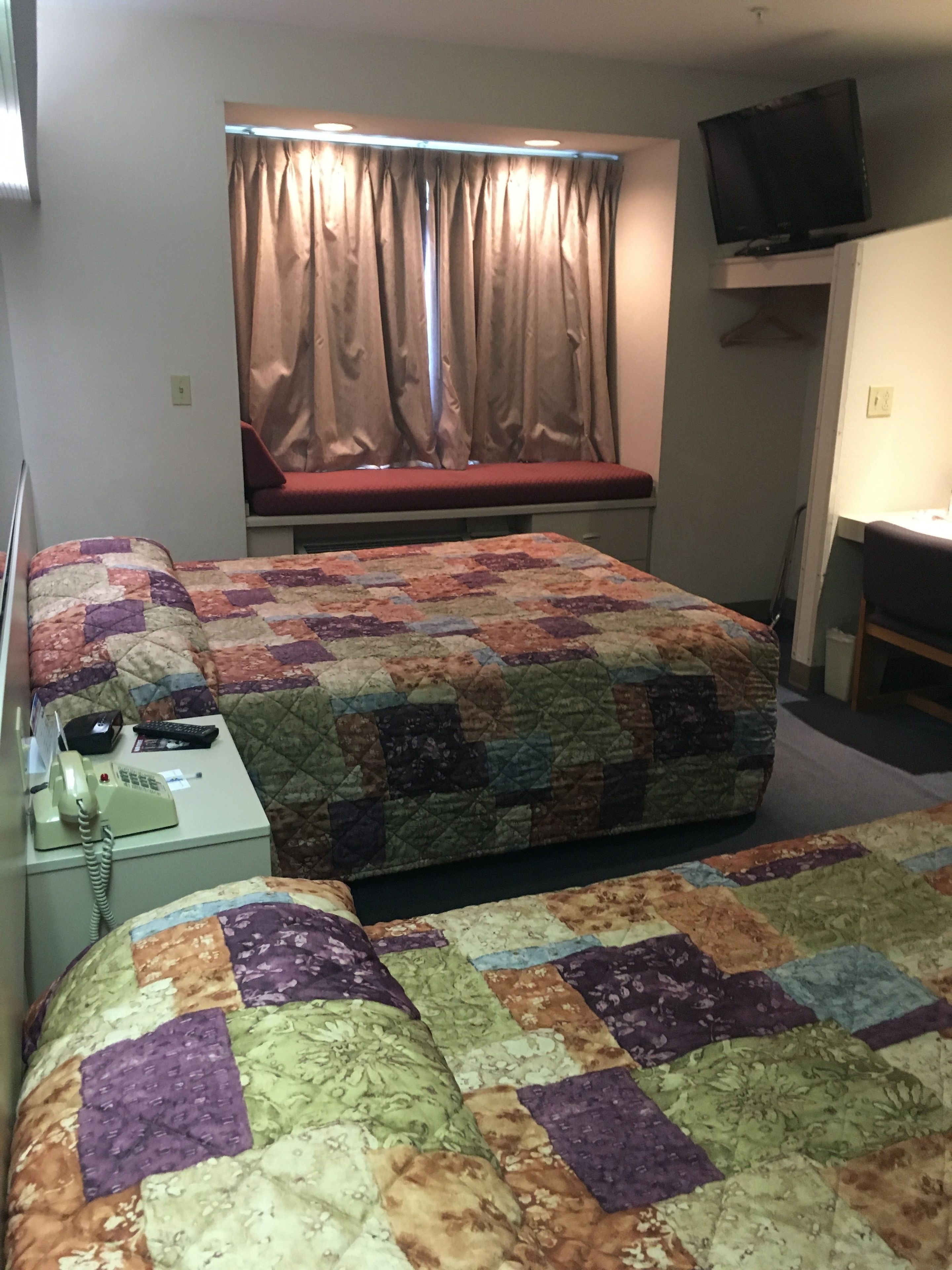 Ein Hotelzimmer mit Bett, Schreibtisch, Stuhl, Fernseher und einem Fenster mit Vorhängen.