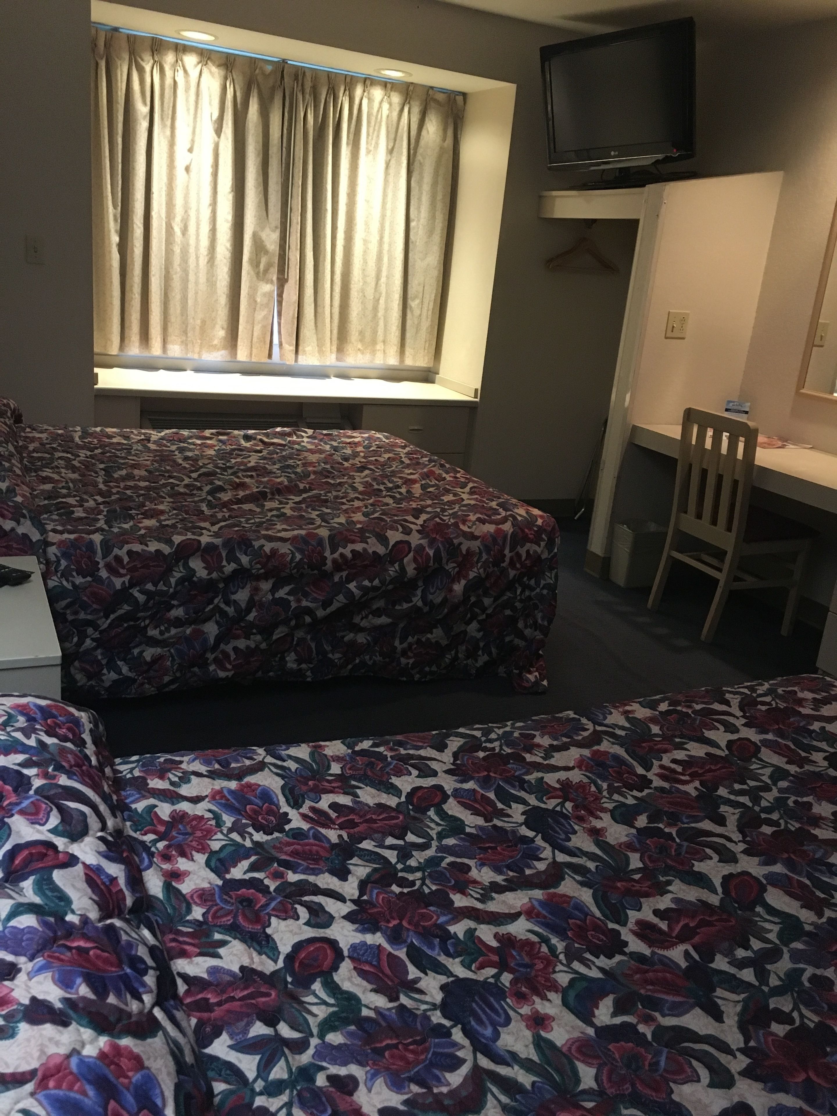 A room with two beds, a desk, a chair, a television, and a window with curtains.