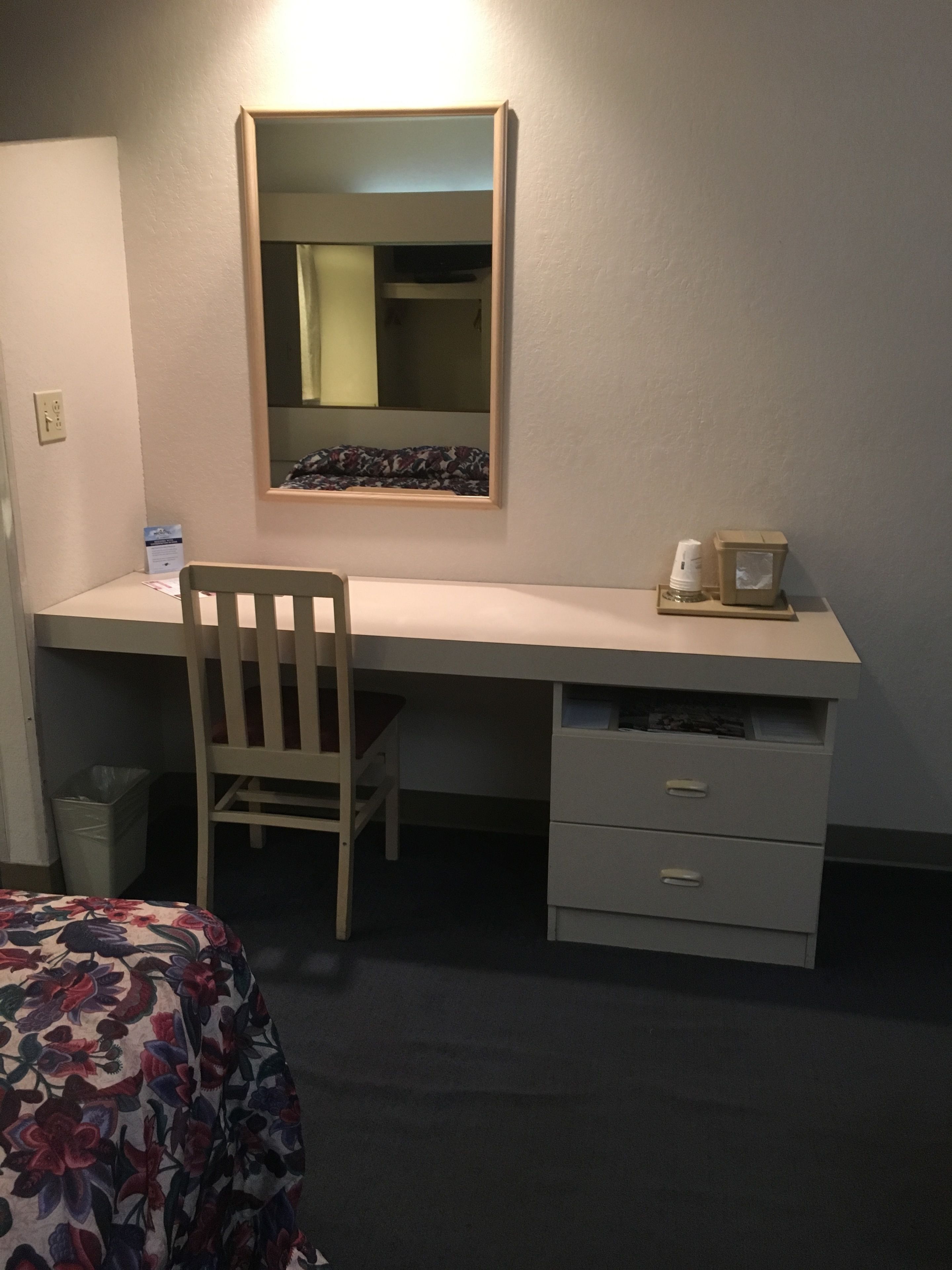 Quarto de hotel com escrivaninha, cadeira e cama com roupa de cama florida.