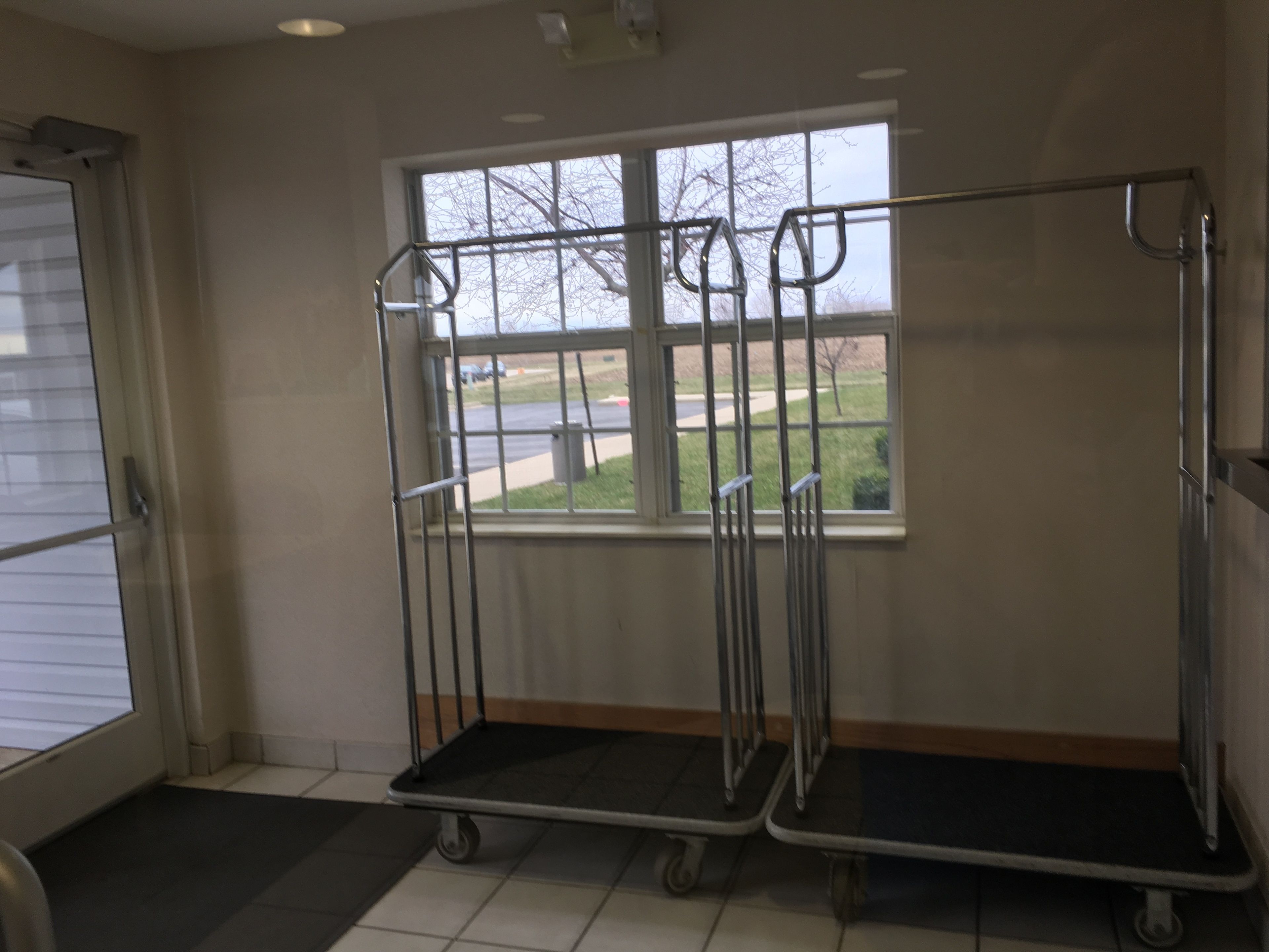 A room with a large window, two metal carts, a door, and a tiled floor.