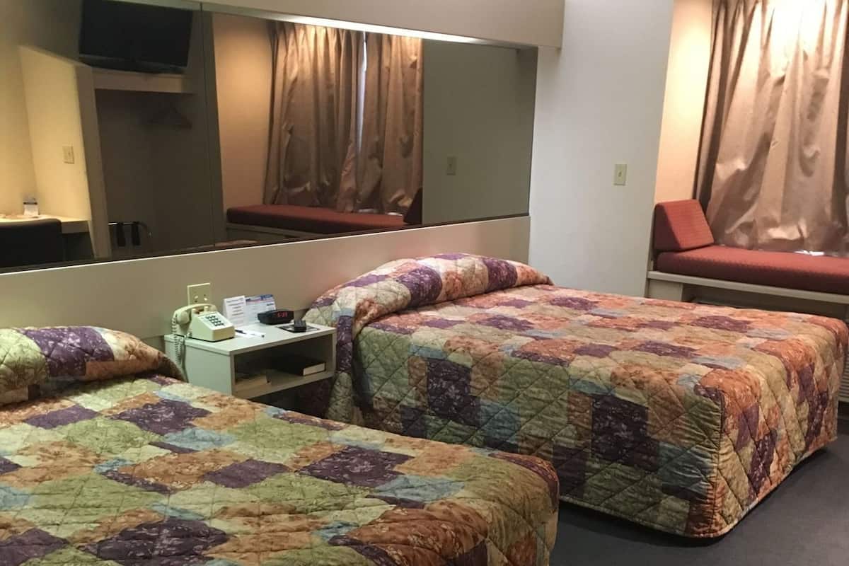 Habitación de hotel con dos camas, un escritorio, teléfono, espejo y televisión.