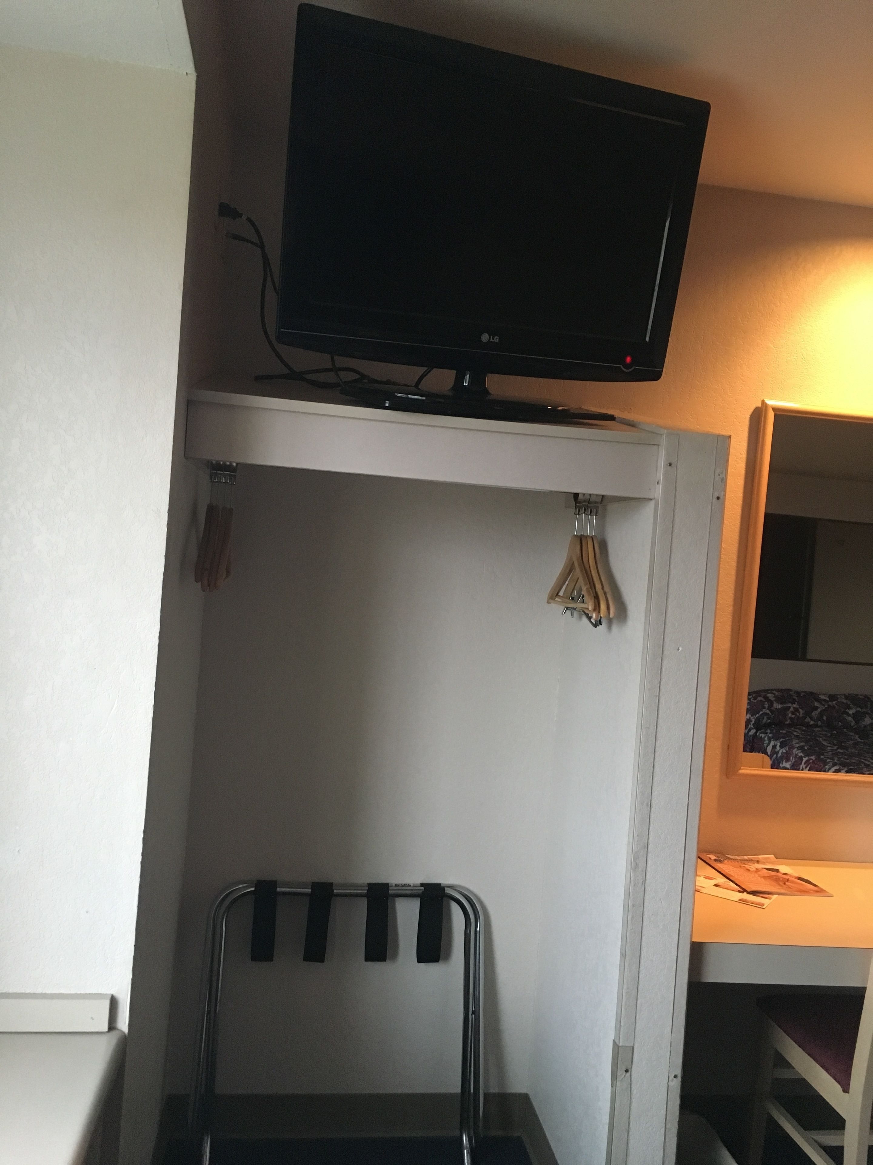 A room with a TV mounted on a white shelf, a metal rack with black straps, and a bunk bed with a patterned blanket.
