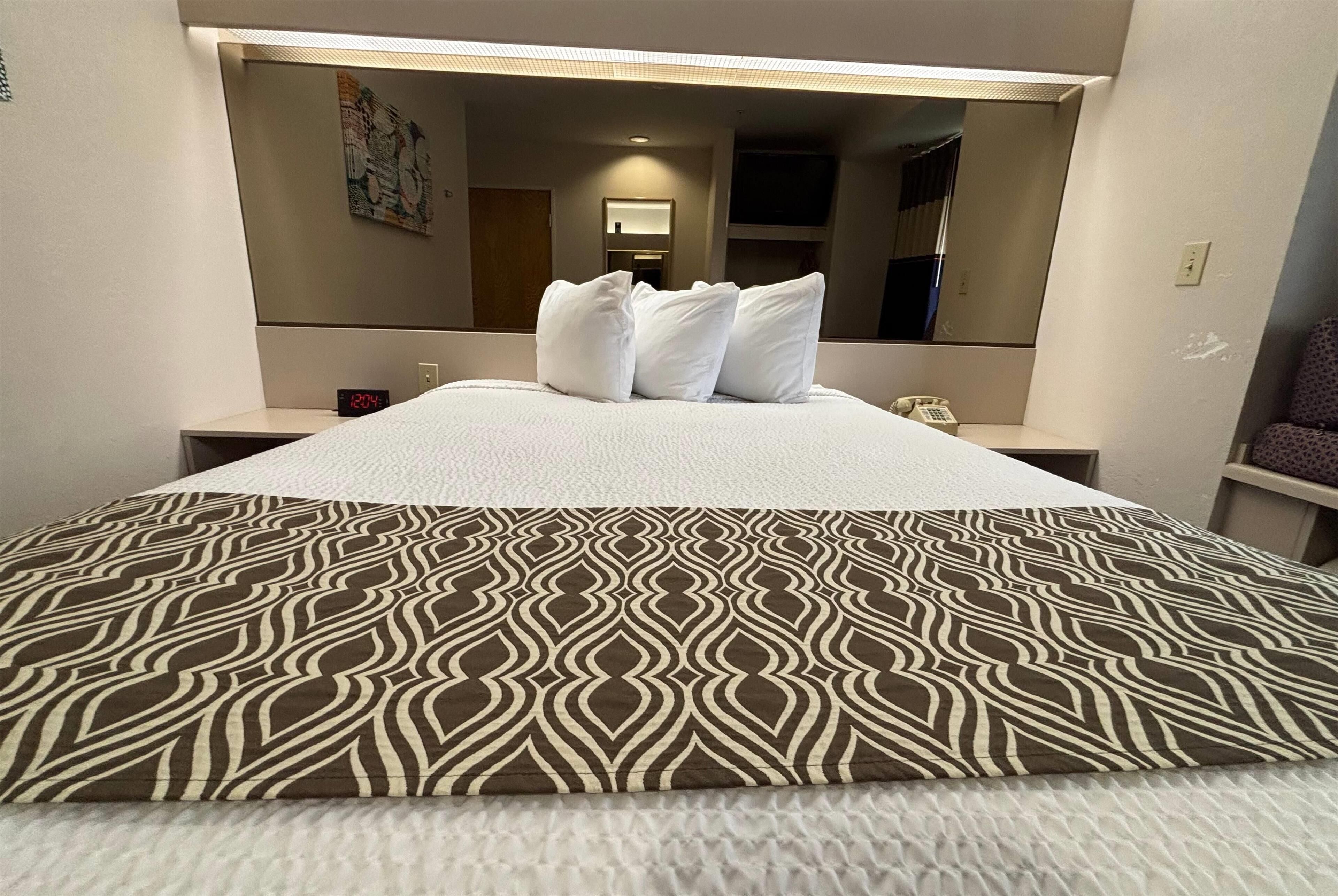Habitació d'hotel amb un llit, una taula de nit, un mirall i un televisor fixat a la paret.
