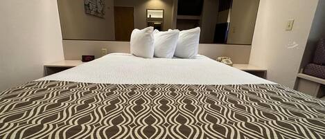 A hotel room with a bed, a bedside table, a mirror, and a wall-mounted TV.