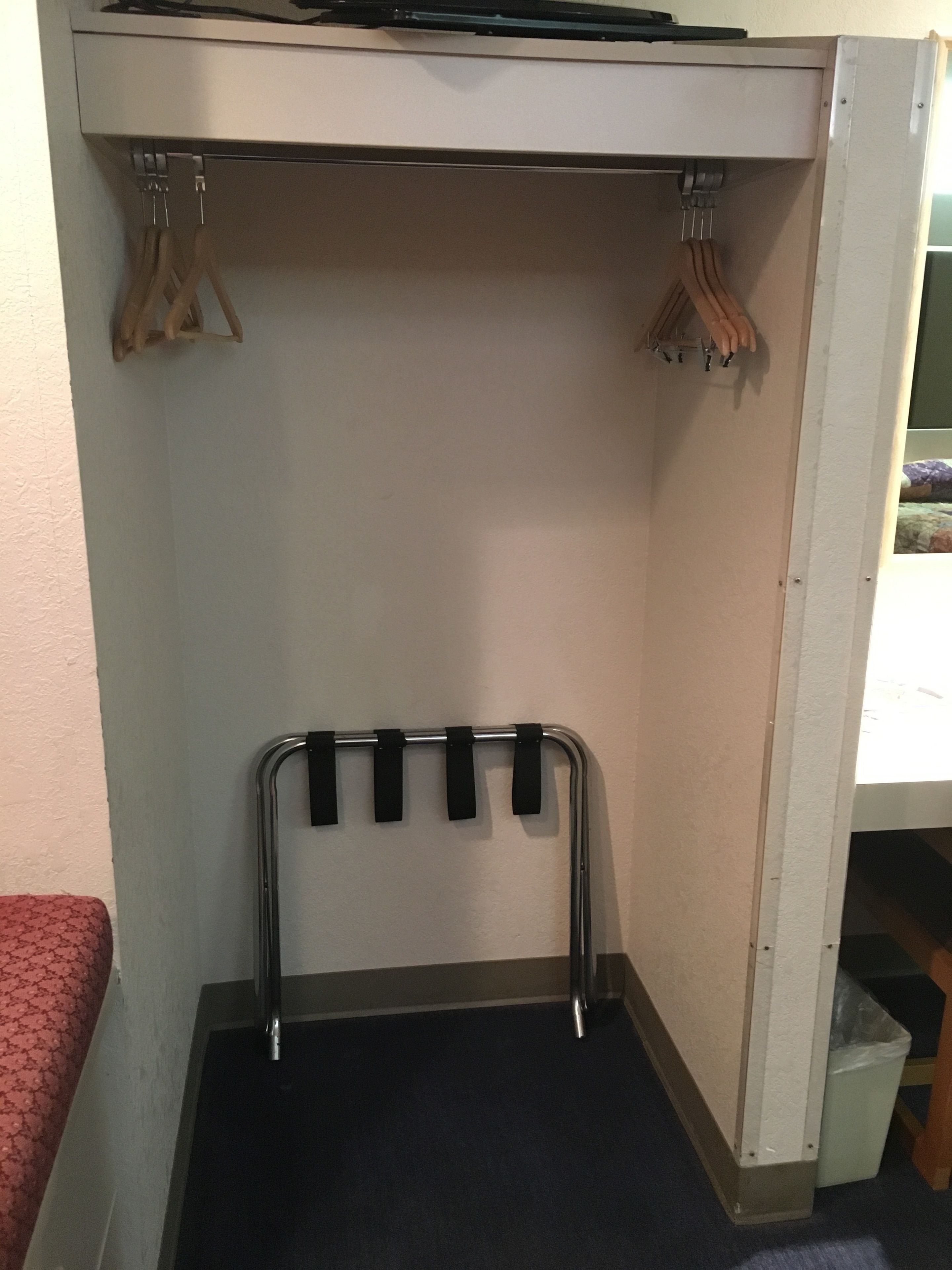 A compact room with a built-in wardrobe, a metal rack with hooks, and a small trash bin.