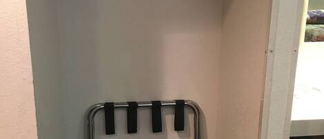 A compact room with a built-in wardrobe, a metal rack with hooks, and a small trash bin.