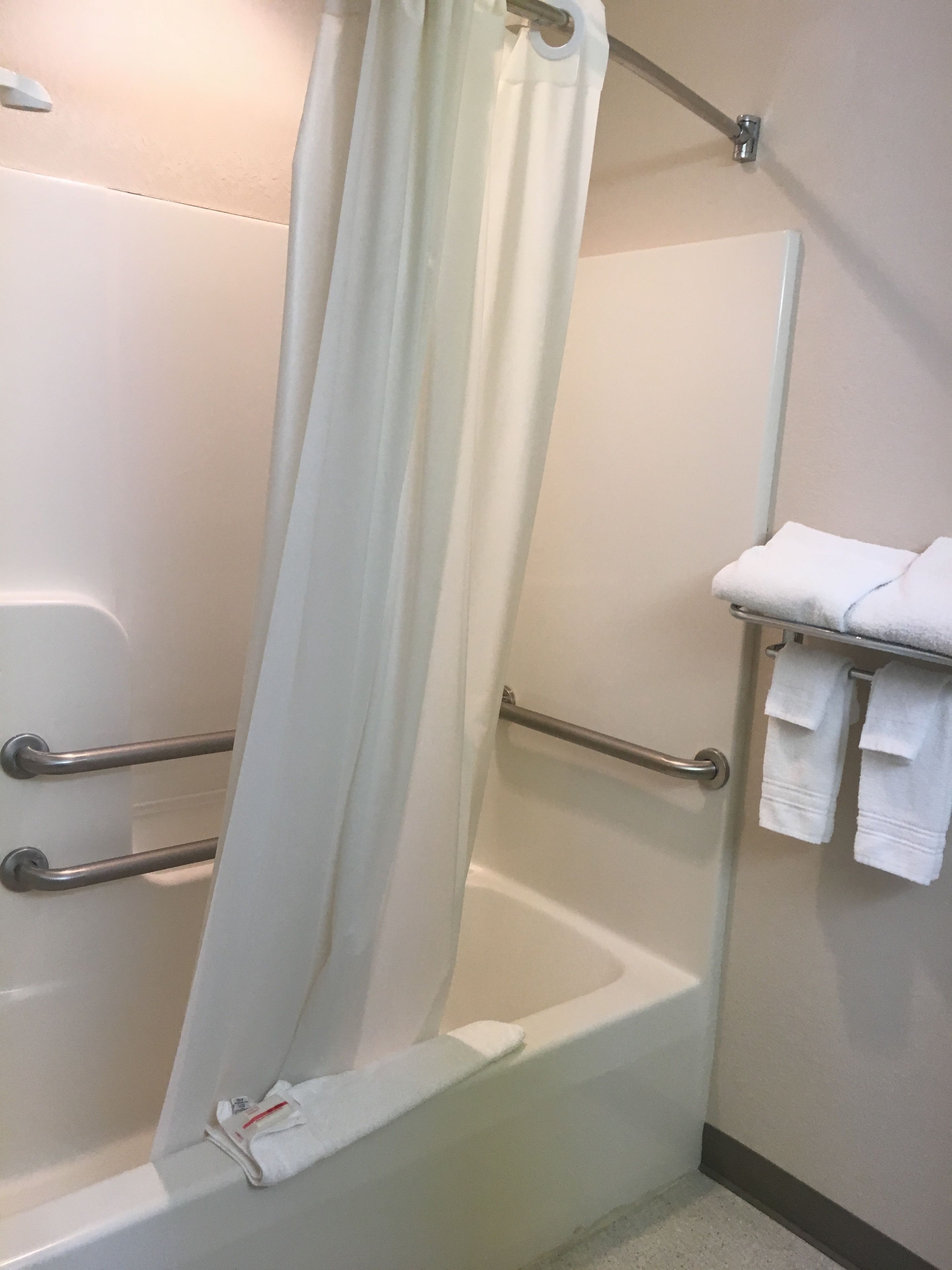 A bathroom with a shower, grab bars, a towel rack, and a toilet.