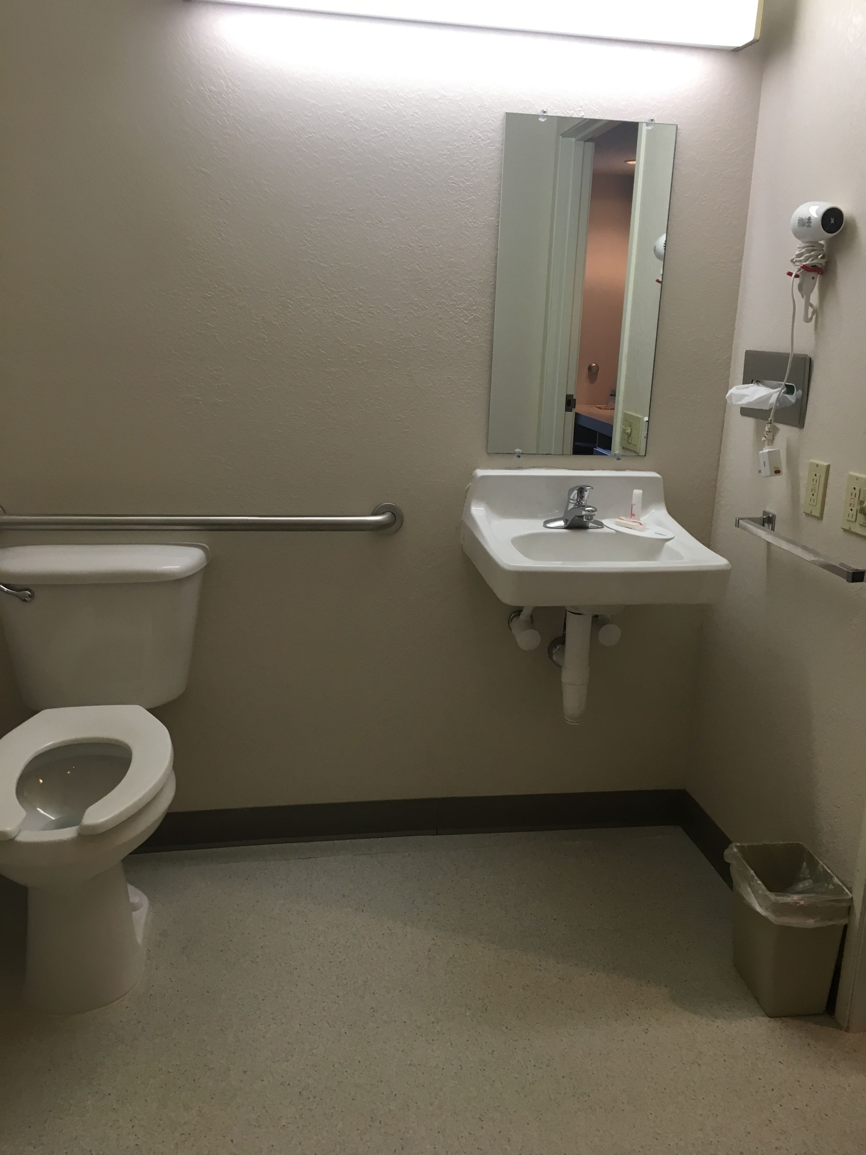 A standard bathroom with a toilet, sink, mirror, and hand dryer.