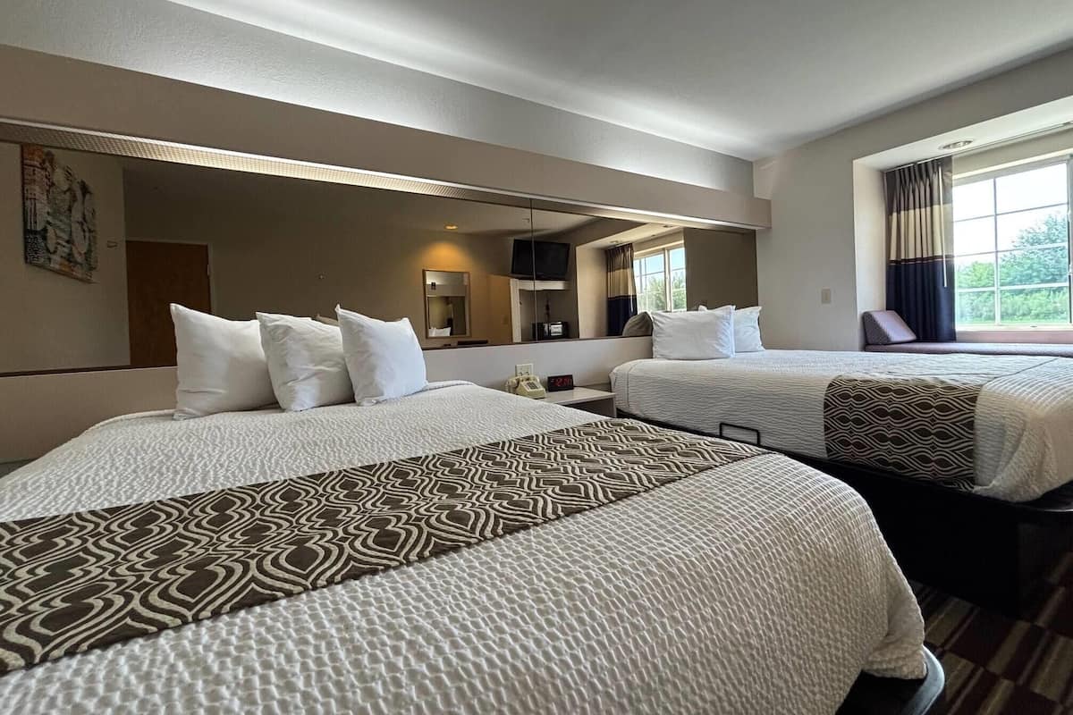 Habitación de hotel con dos camas, un espejo grande, un televisor y una ventana con cortinas.