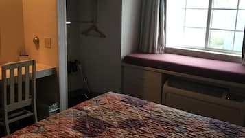Una camera da letto con un letto, una TV a parete, una finestra con tende e un termosifone.