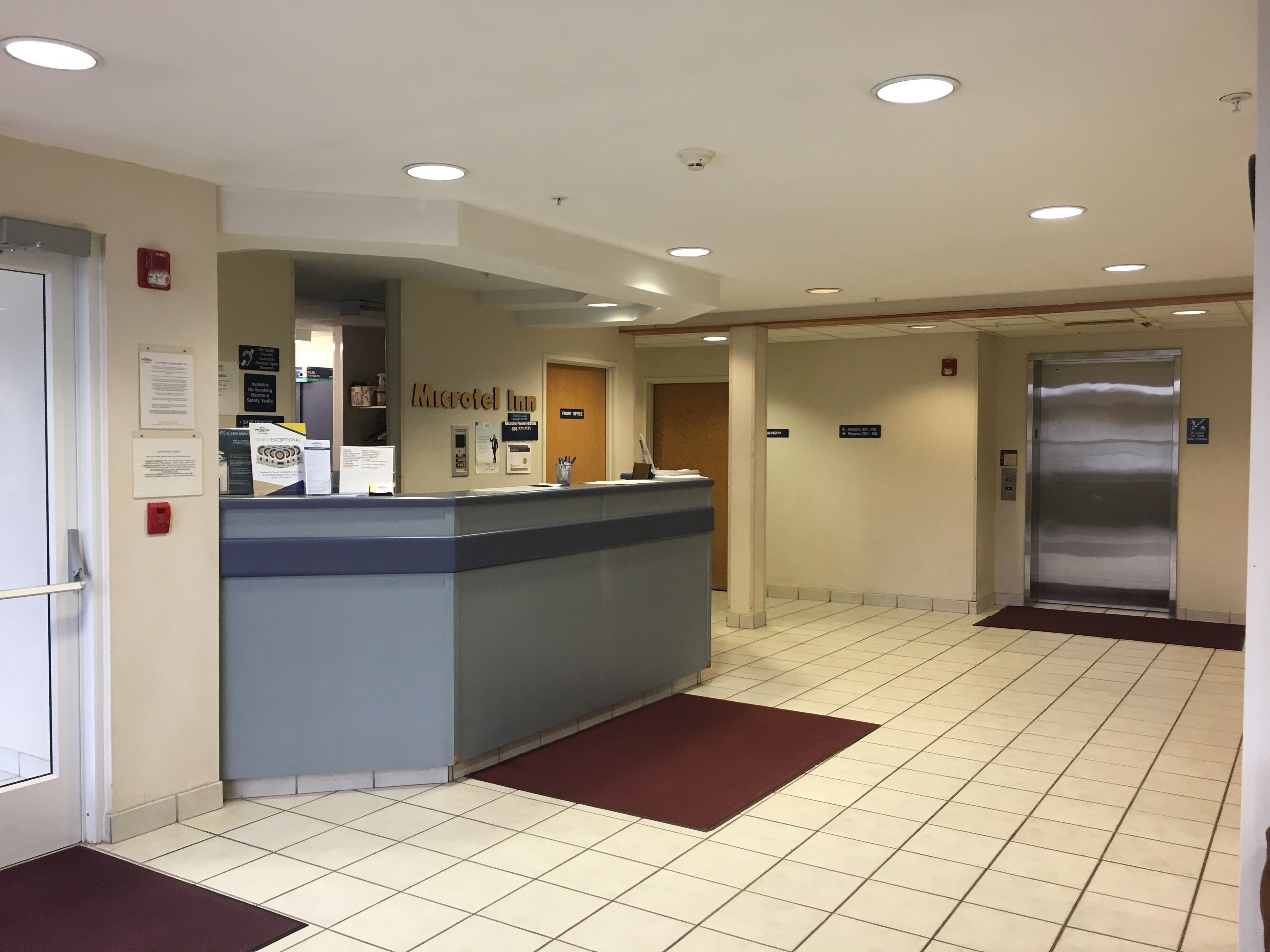 A hotel reception area with a reception desk, a fire alarm, and an elevator.