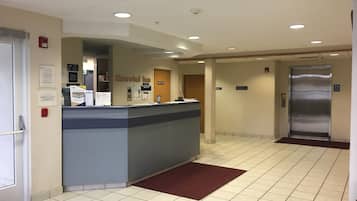 A hotel reception area with a reception desk, a fire alarm, and an elevator.