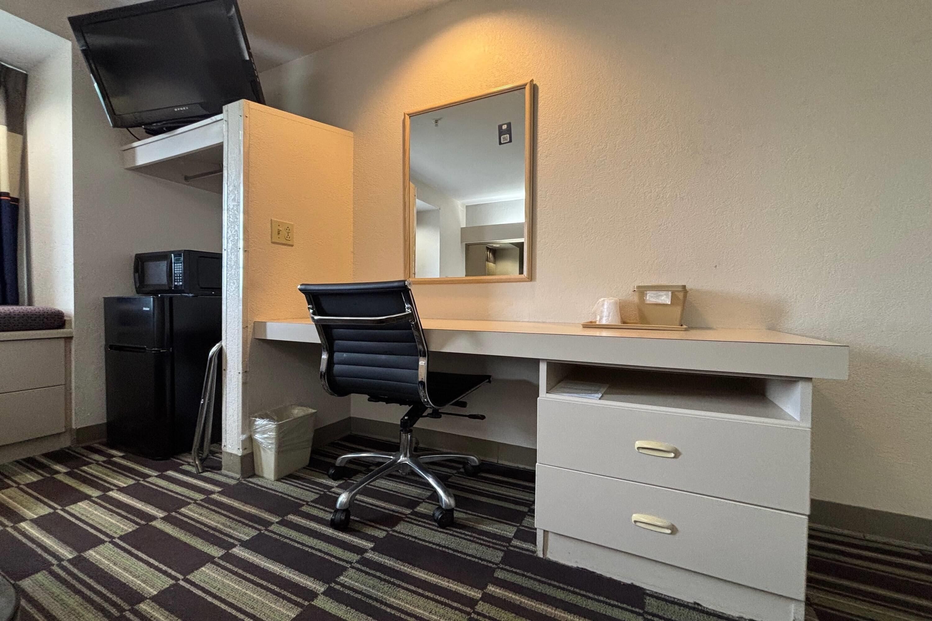 Habitación de hotel con escritorio, silla, televisor, microondas, refrigerador y espejo.