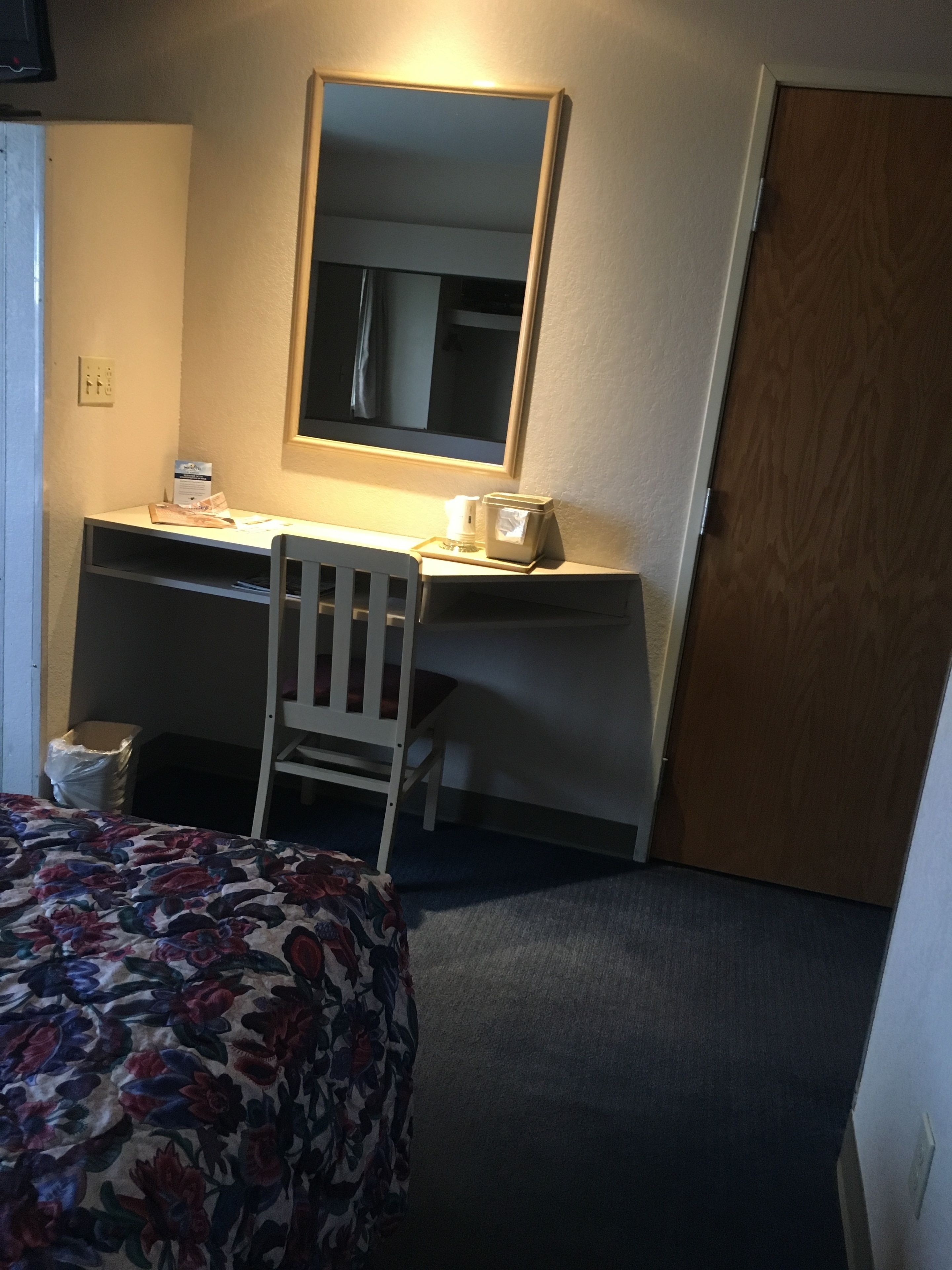 Una camera d'albergo con un letto, una scrivania con una sedia, uno specchio e una porta.
