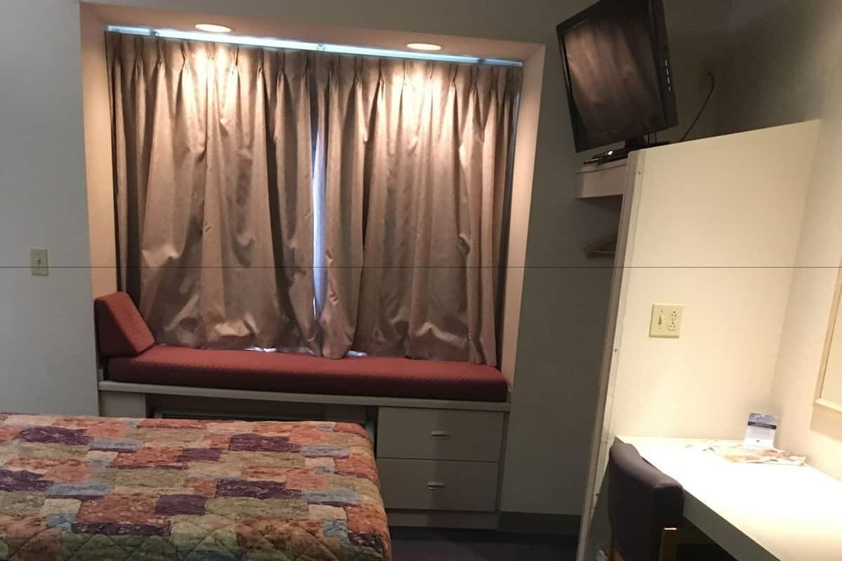 Una habitación con dos camas, un escritorio, una silla, un televisor y una ventana con cortinas.
