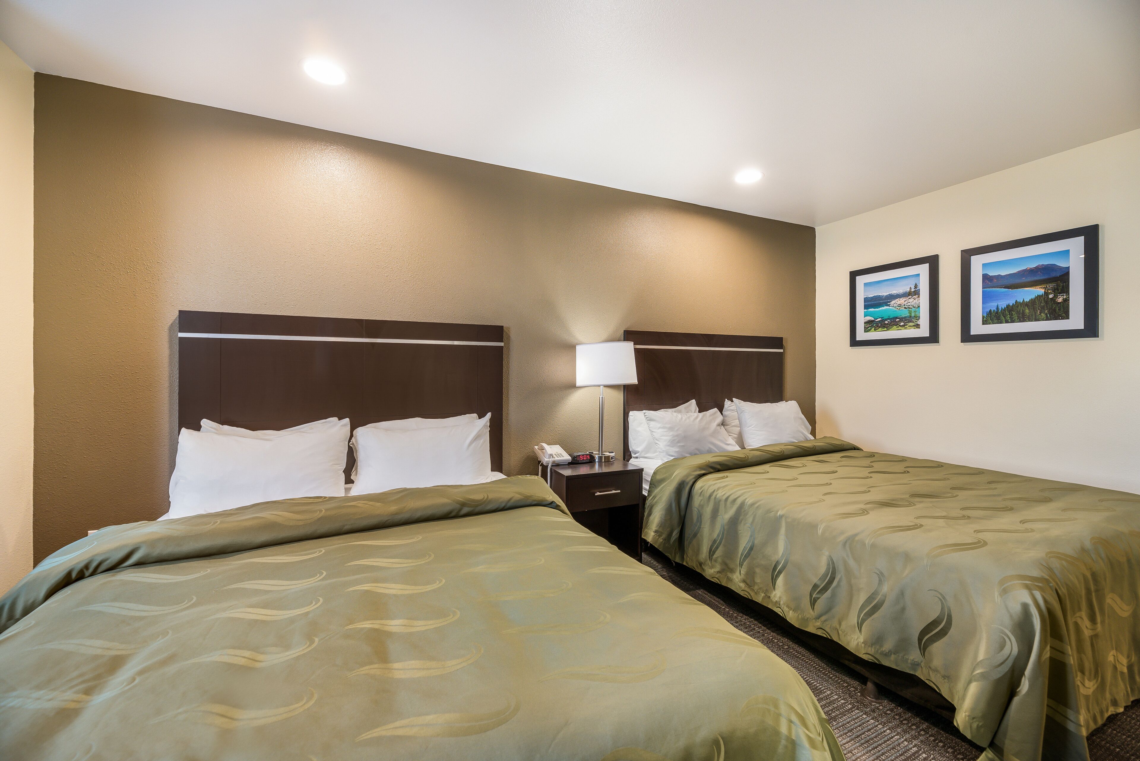 A hotel room with two single beds, a nightstand with a lamp, and two framed pictures on the wall.