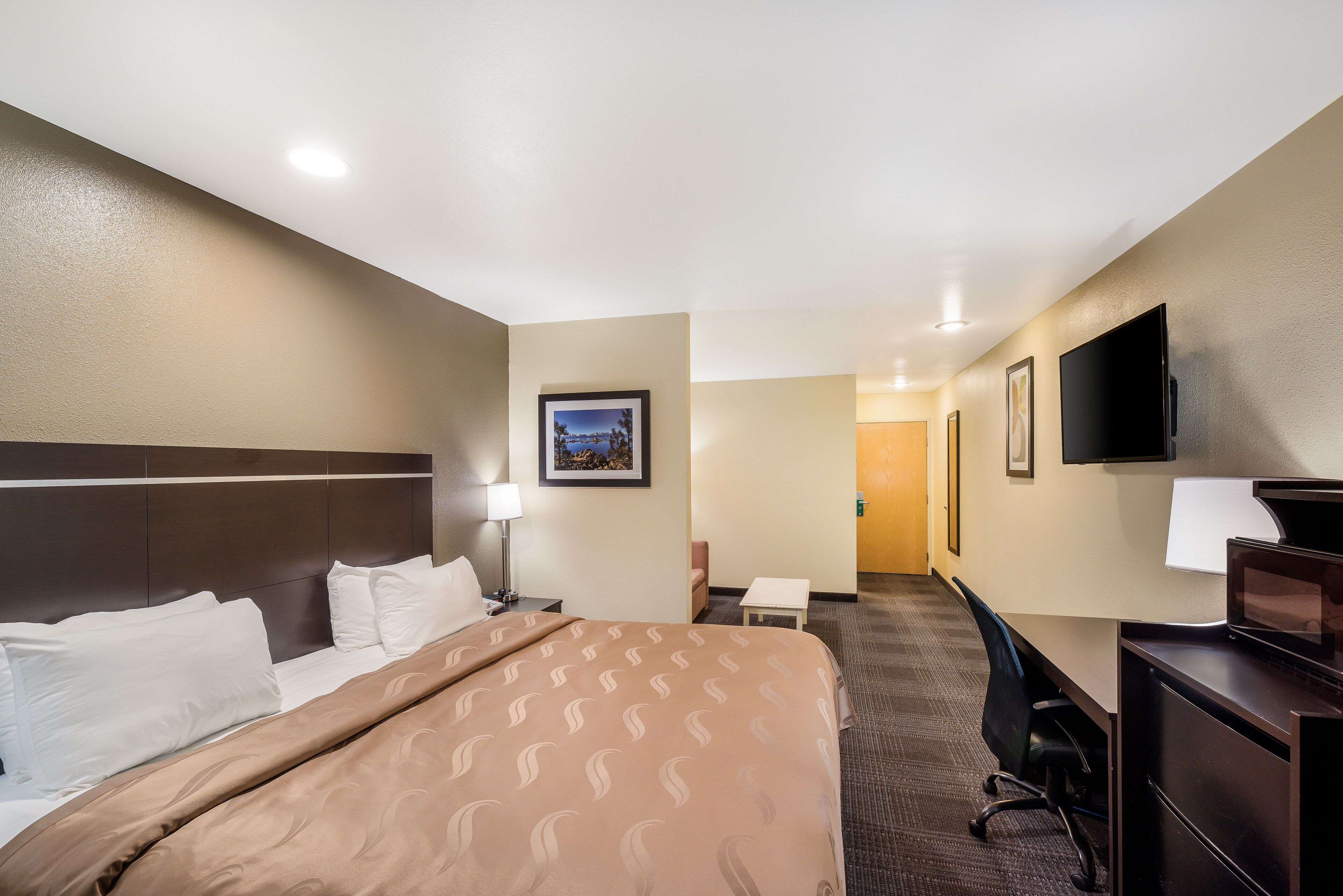 A hotel room with a bed, desk, chair, and a television.