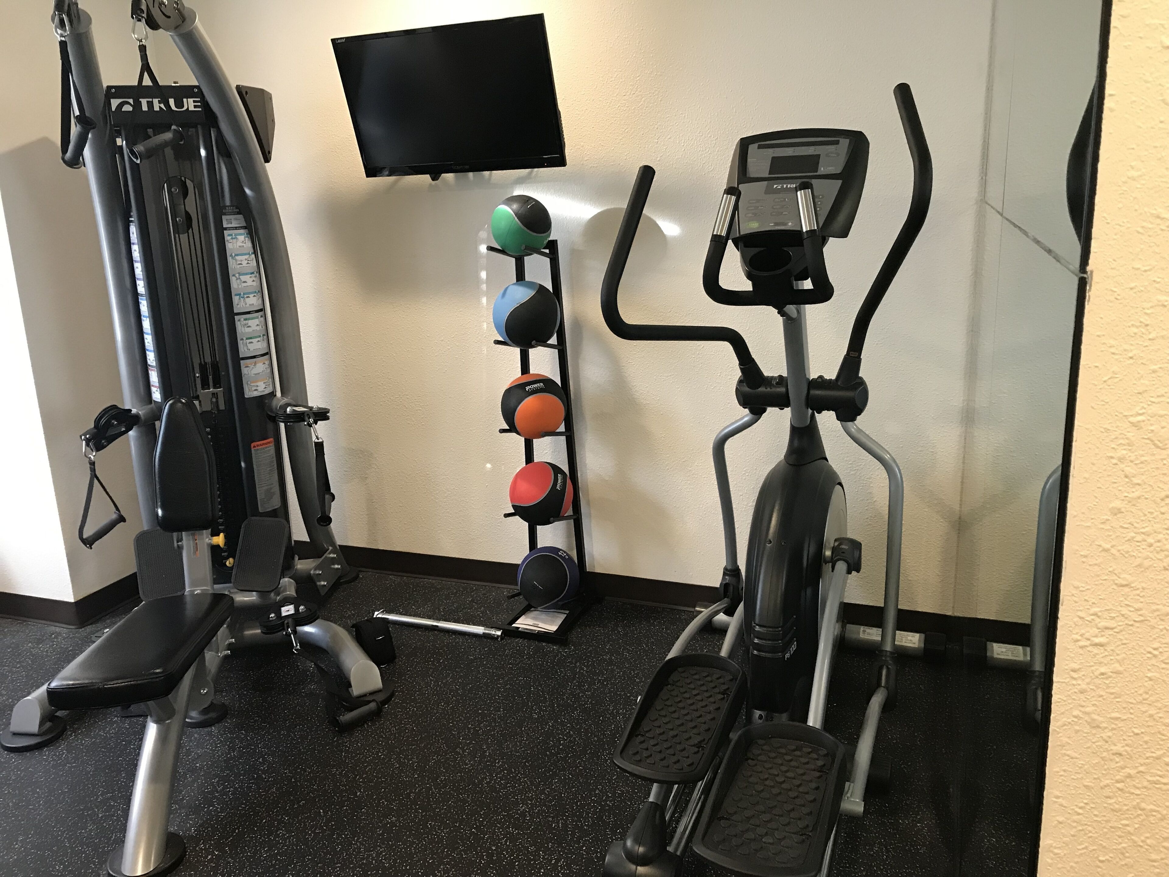 Een sportschool met een hometrainer, een crosstrainer en een krachttrainingapparaat.