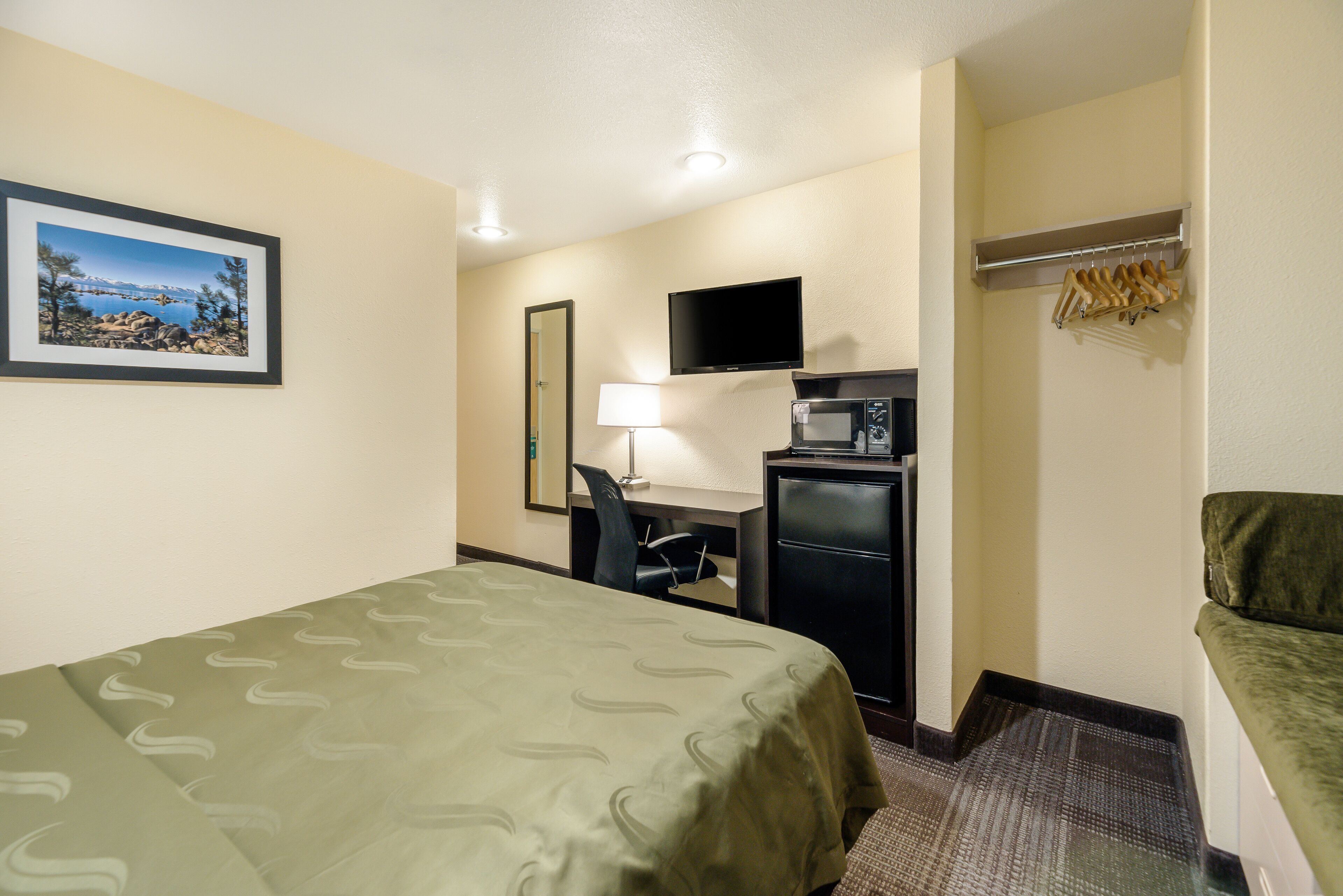 Una habitación de hotel con cama, escritorio, silla, televisor y perchero.