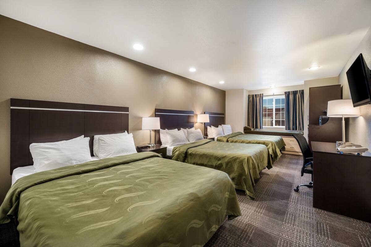 A hotel room with two beds, a desk, a TV, and a window with curtains.
