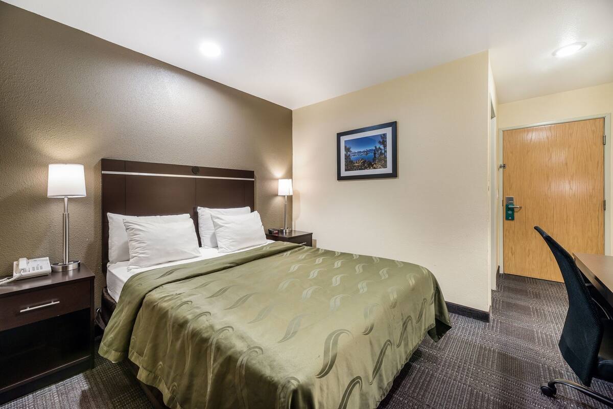 A hotel room with a bed, bedside lamps, a desk, and a door.
