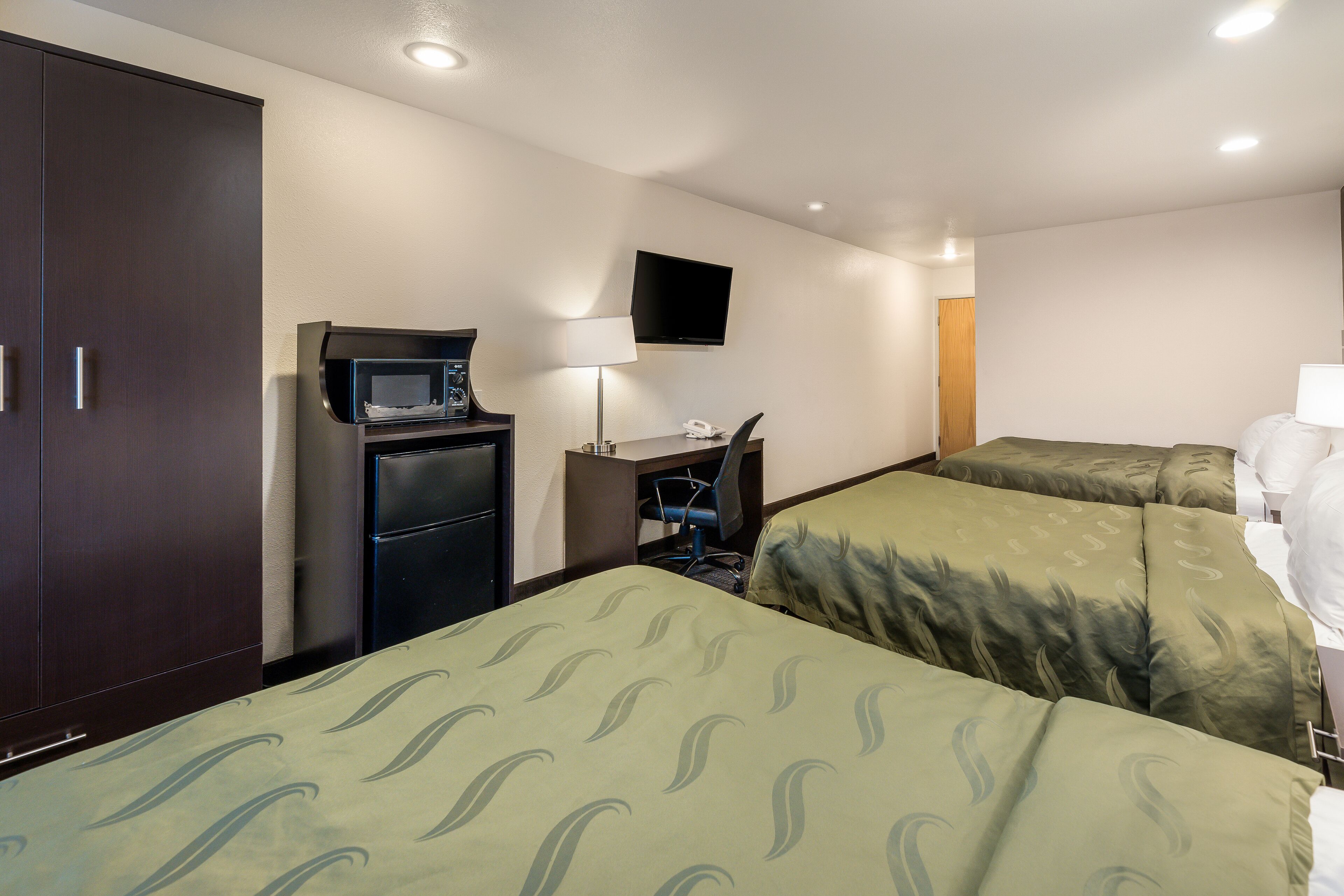 Habitación de hotel con dos camas individuales, un escritorio con ordenador, microondas y televisor en la pared.