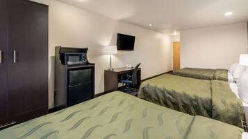 Habitación de hotel con dos camas individuales, un escritorio con ordenador, microondas y televisor en la pared.