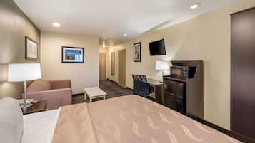 Habitación de hotel con cama, escritorio, silla, televisión, microondas y puerta.