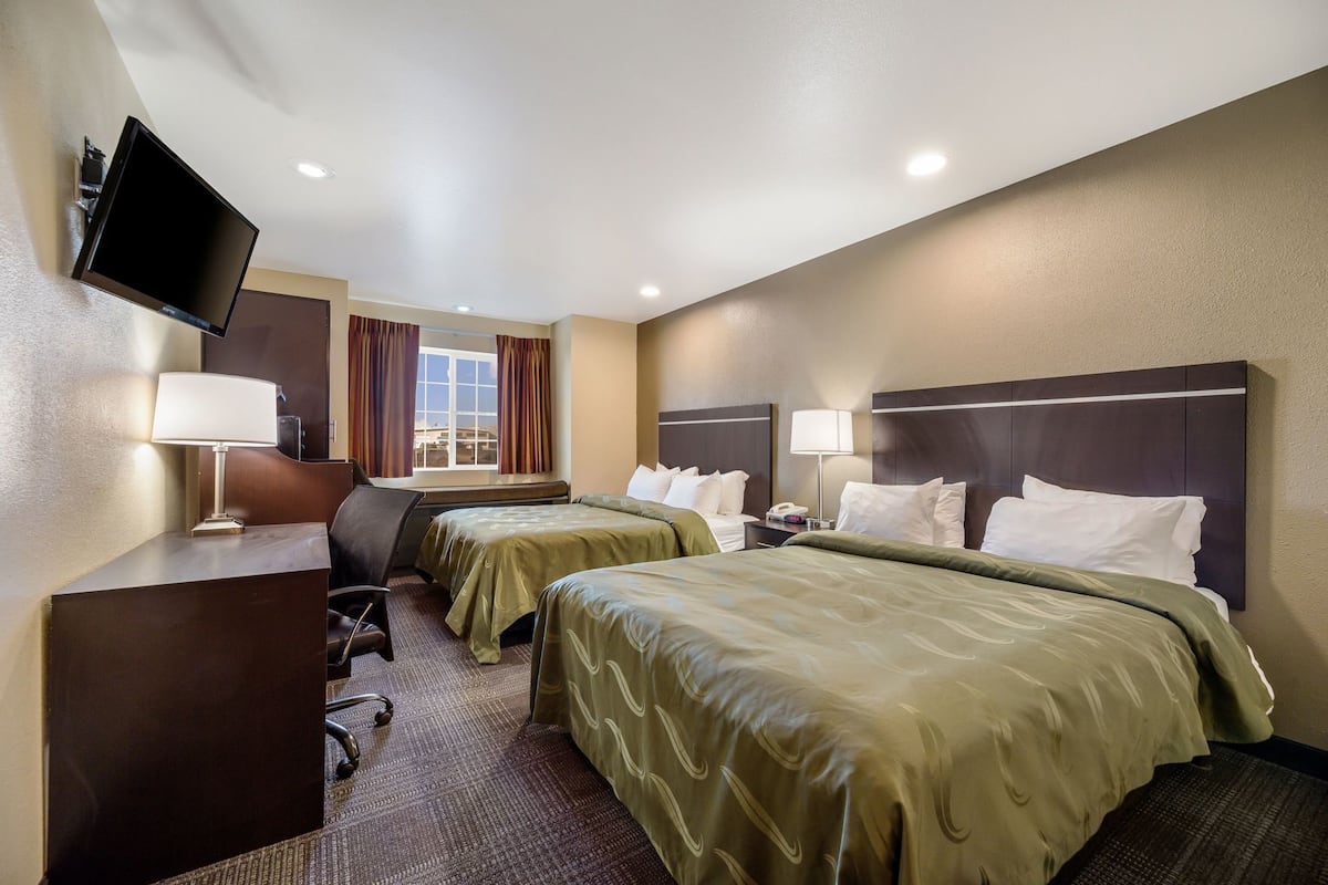 A hotel room with two beds, a desk, a TV, and a window with curtains.