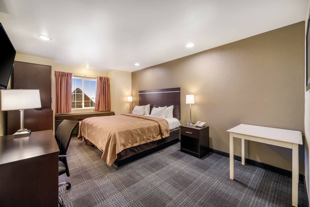 A hotel room with a bed, bedside tables, a desk, a chair, and a TV.