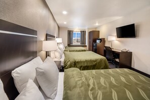 A hotel room with two beds, a desk, a chair, a television, and a window with curtains.