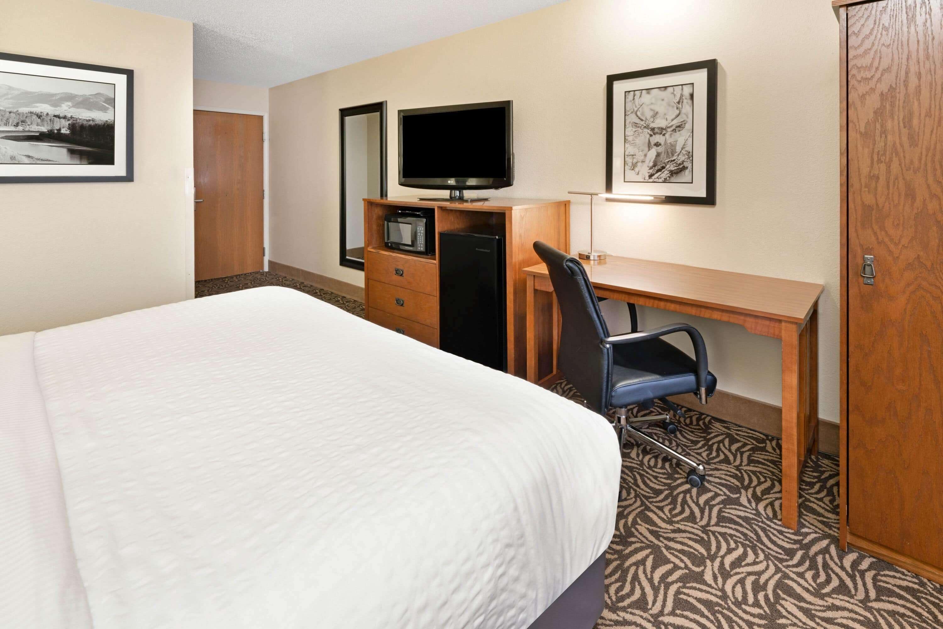 A hotel room with a bed, a desk with a computer, a television, and a microwave.