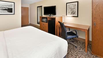 Una habitación de hotel con una cama, un escritorio con computadora, televisión y microondas.