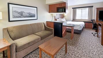A hotel room with a sofa, a small wooden table, a bed, a desk, a microwave, and a television.