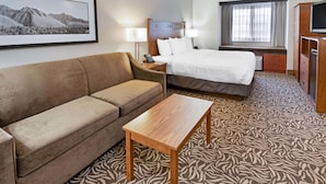 A hotel room with a bed, a sofa, a wooden table, a TV, and a window with curtains. - La Quinta Inn by Wyndham Missoula (Missoula)