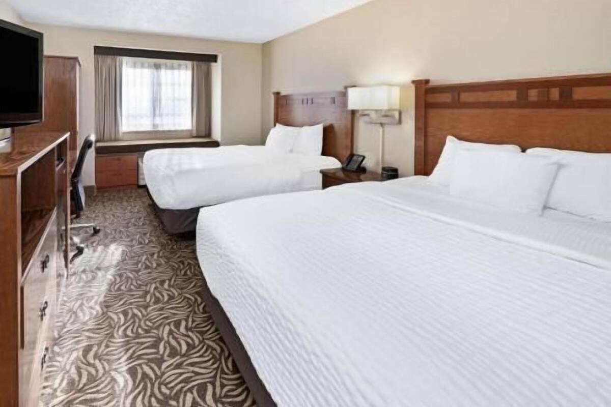A hotel room with two beds, a TV, a desk, and a window with curtains.