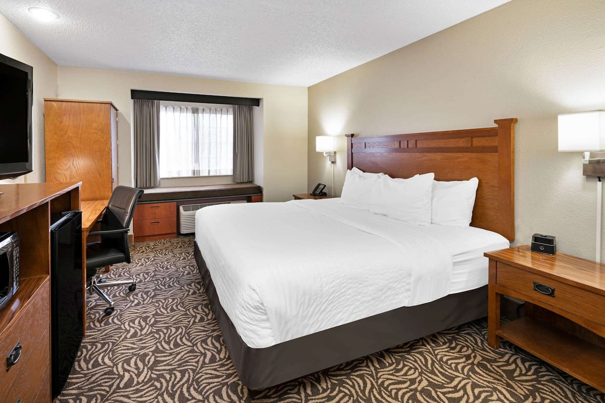 A hotel room with a large bed, a desk with a chair, a television, and a window with curtains.